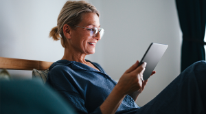 Close up shot of an older woman sitting and relaxing in her pajamas in the bed at home and reading from a tablet